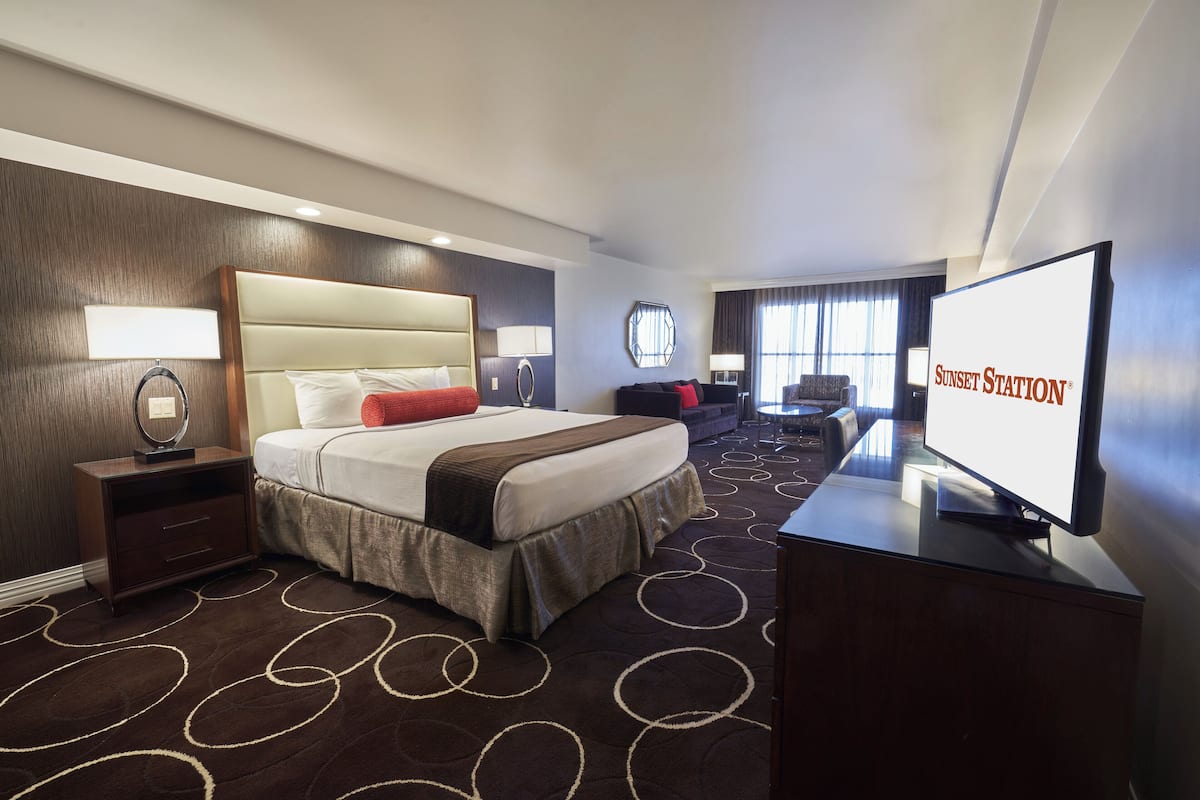 Ein Hotelzimmer mit einem großen Bett, einem Fernseher, einem Schreibtisch und Blick auf die Stadt.