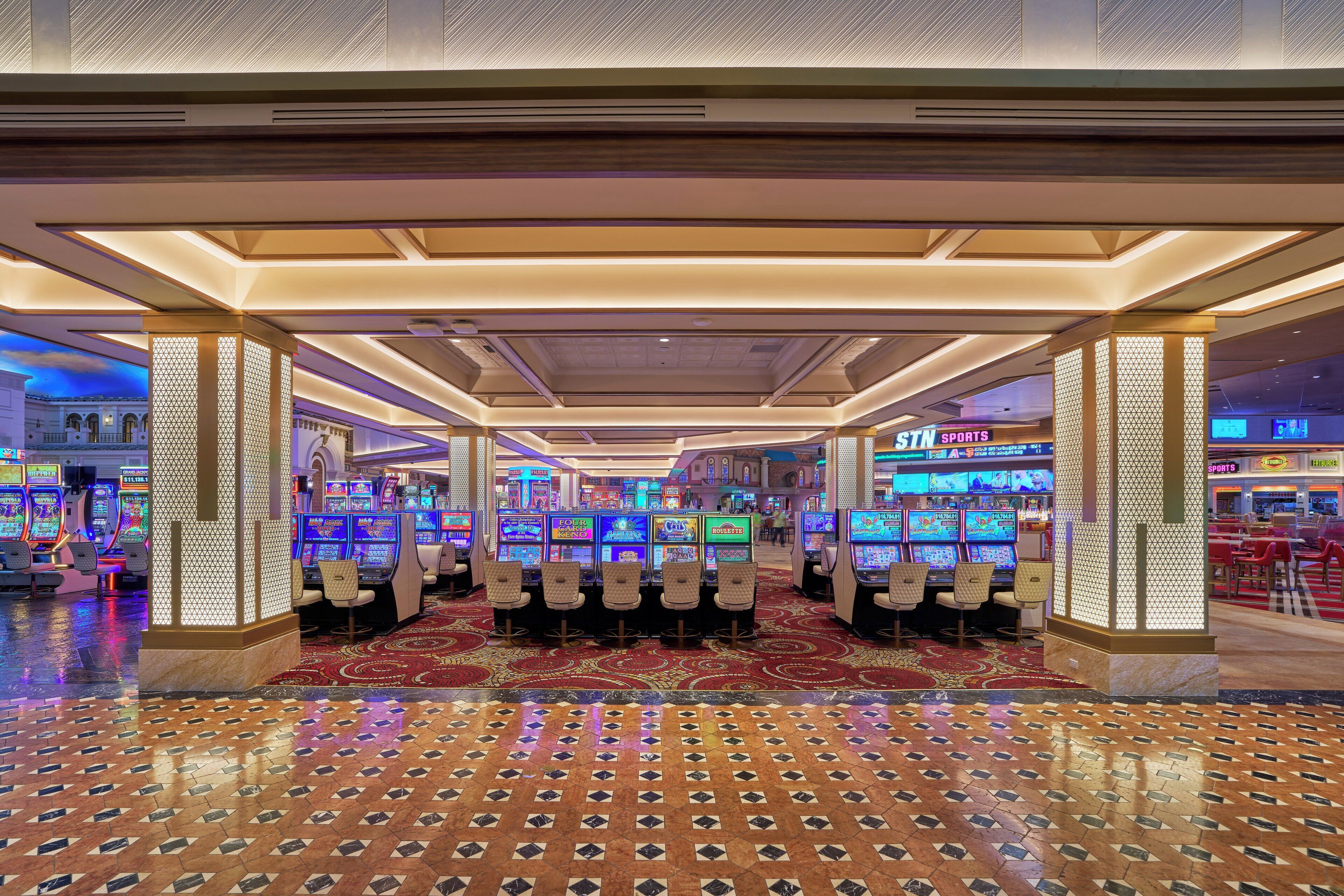 Ein Casino mit Spielautomaten, einem gemusterten Teppich und einer Decke mit eingelassener Beleuchtung.