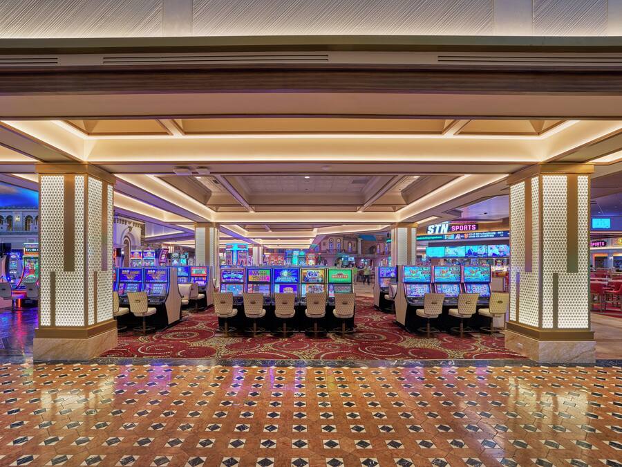 Ein Casino mit Spielautomaten, einem gemusterten Teppich und einer Decke mit eingelassener Beleuchtung.