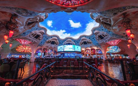 A bar with a unique architectural design, featuring a ceiling that resembles a sky with clouds and a large circular stained glass window.