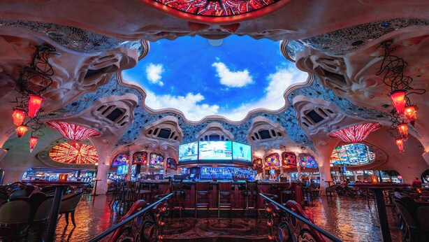 Un bar au design architectural unique, avec un plafond évoquant un ciel nuageux et une grande fenêtre circulaire en vitrail.