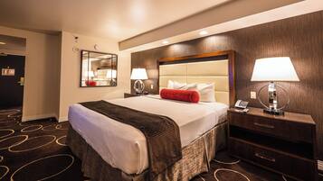 A hotel room with a large bed, two bedside tables with lamps, a wooden headboard, a mirror, and a carpet with a circular pattern.