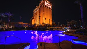 Un hôtel doté d’une piscine éclairée la nuit, avec un grand bâtiment sur lequel on peut lire l’inscription « Sunset Station ».