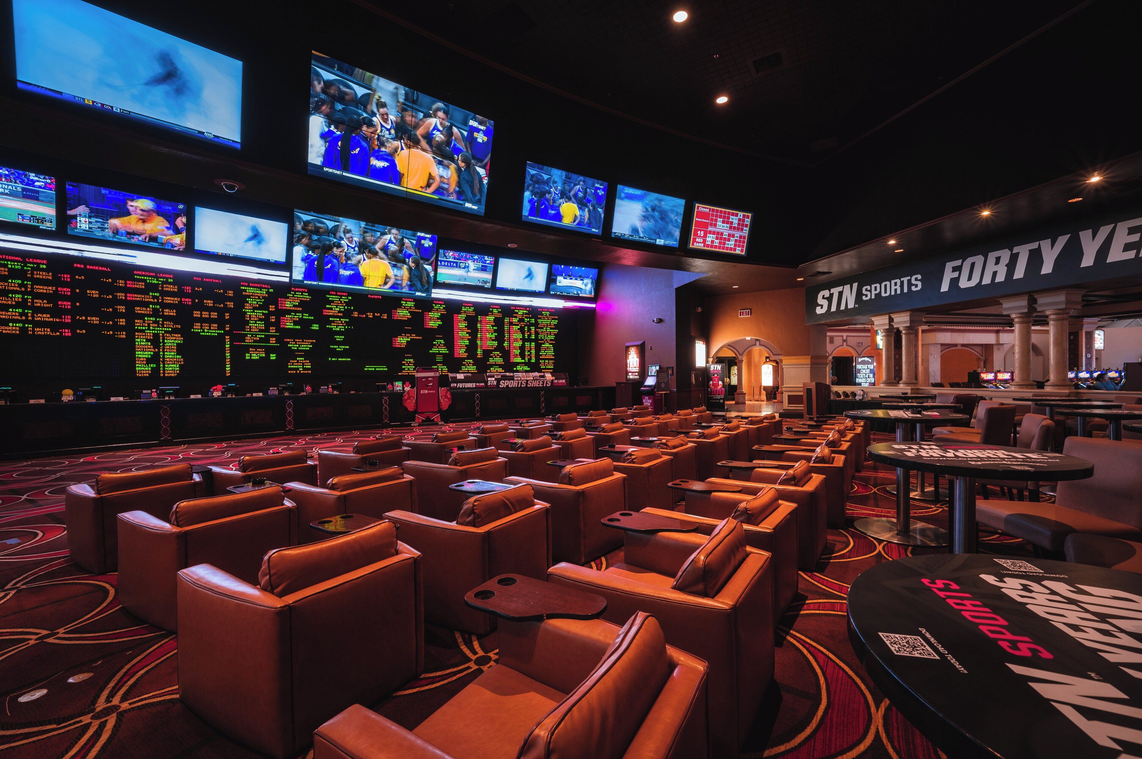 Un casinò con diverse schermi che mostrano eventi sportivi, zone relax con sedute in pelle e un cartello per STN Sports.