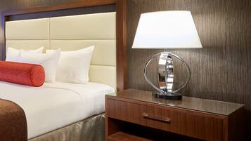A neatly made bed with white linens and a red throw pillow, a bedside table with a lamp, and a wooden headboard.