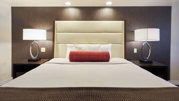 A hotel room with a large bed, two bedside lamps, a red throw pillow, and a wooden headboard.