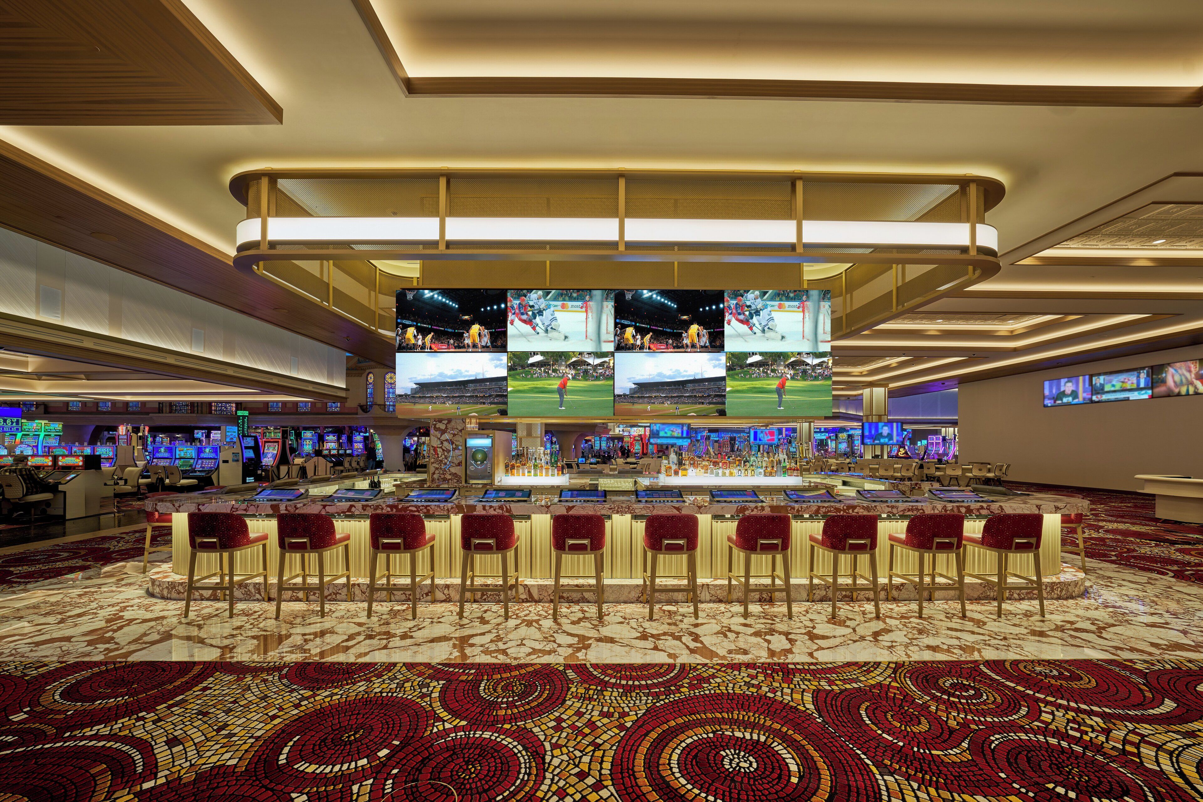 Un casinò con diverse schermate, zona bar e pavimento con tappeto rosso.