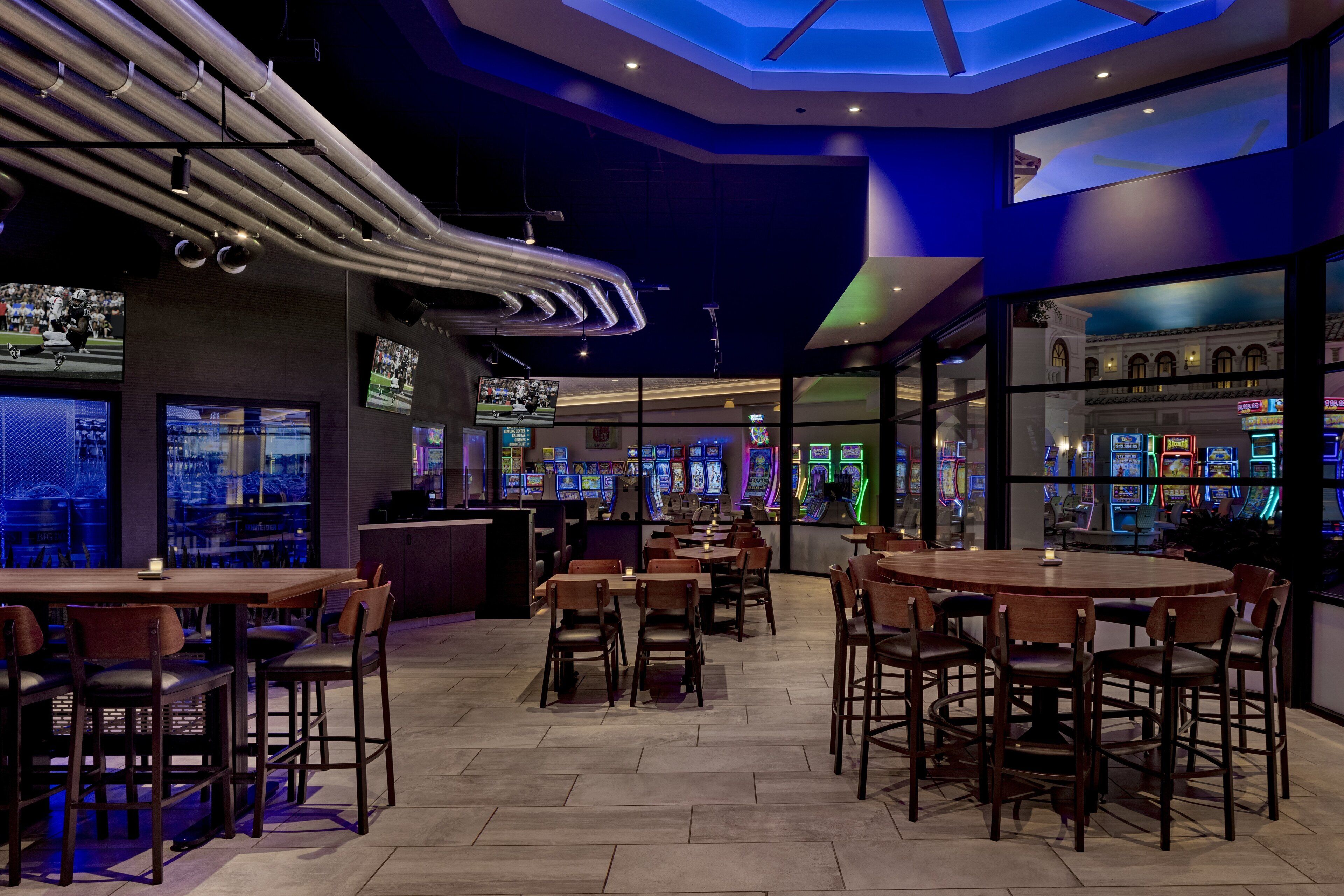 A modern bar area with multiple gaming machines, wooden tables, and chairs.