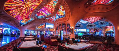 L’intérieur d’un casino, avec de magnifiques vitraux colorés au plafond, de nombreuses tables de jeux et une grande variété de machines à sous.