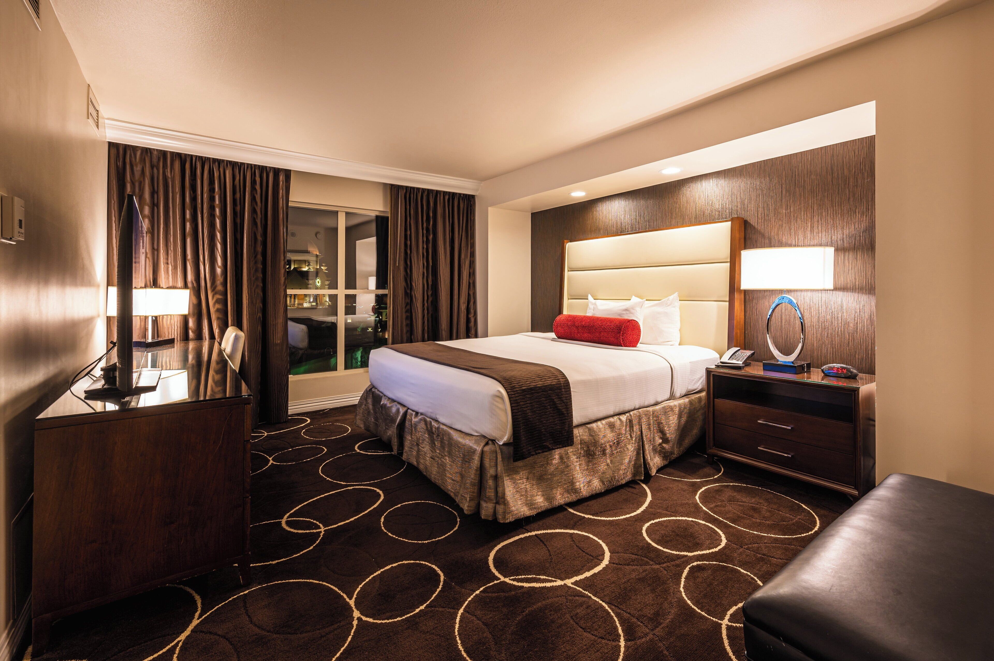 Habitación de hotel con cama, escritorio, silla, mesita de noche y vista a la ciudad.