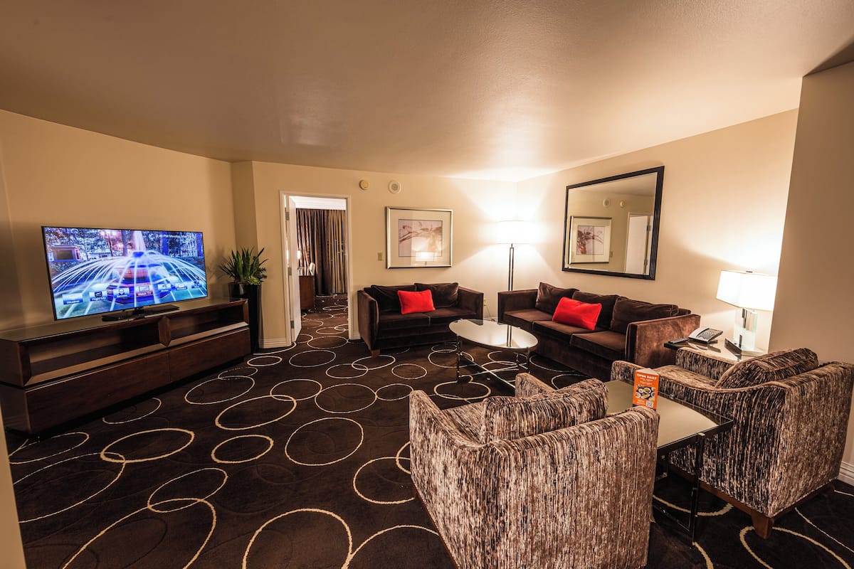 Ein Hotel-Wohnzimmer mit einem Flachbildfernseher, zwei Sofas, einem Couchtisch und einem gemusterten Teppich.