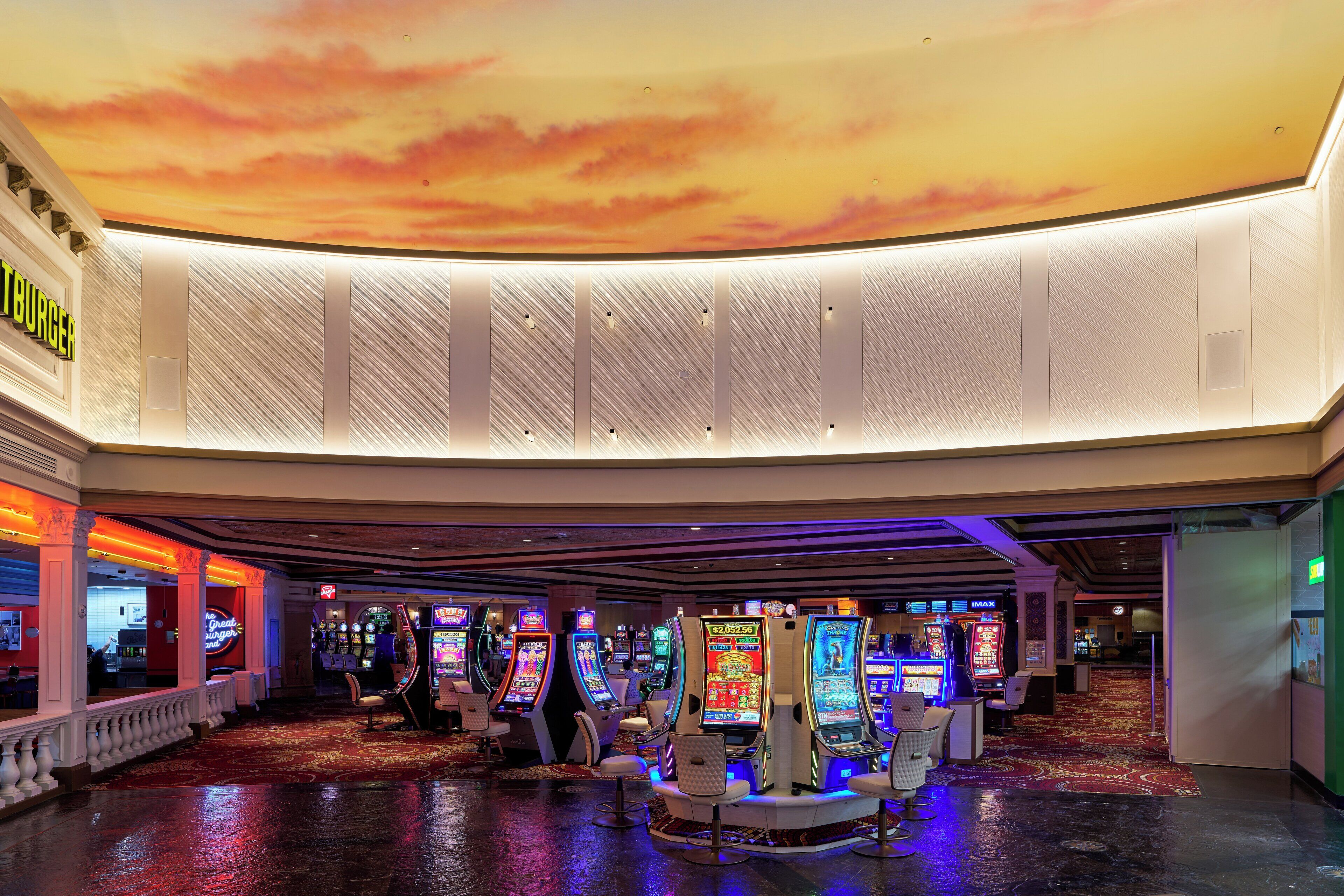 Ein Kasino mit Spielautomaten, einer Bar und einer Decke mit Sonnenuntergangsmotiv.
