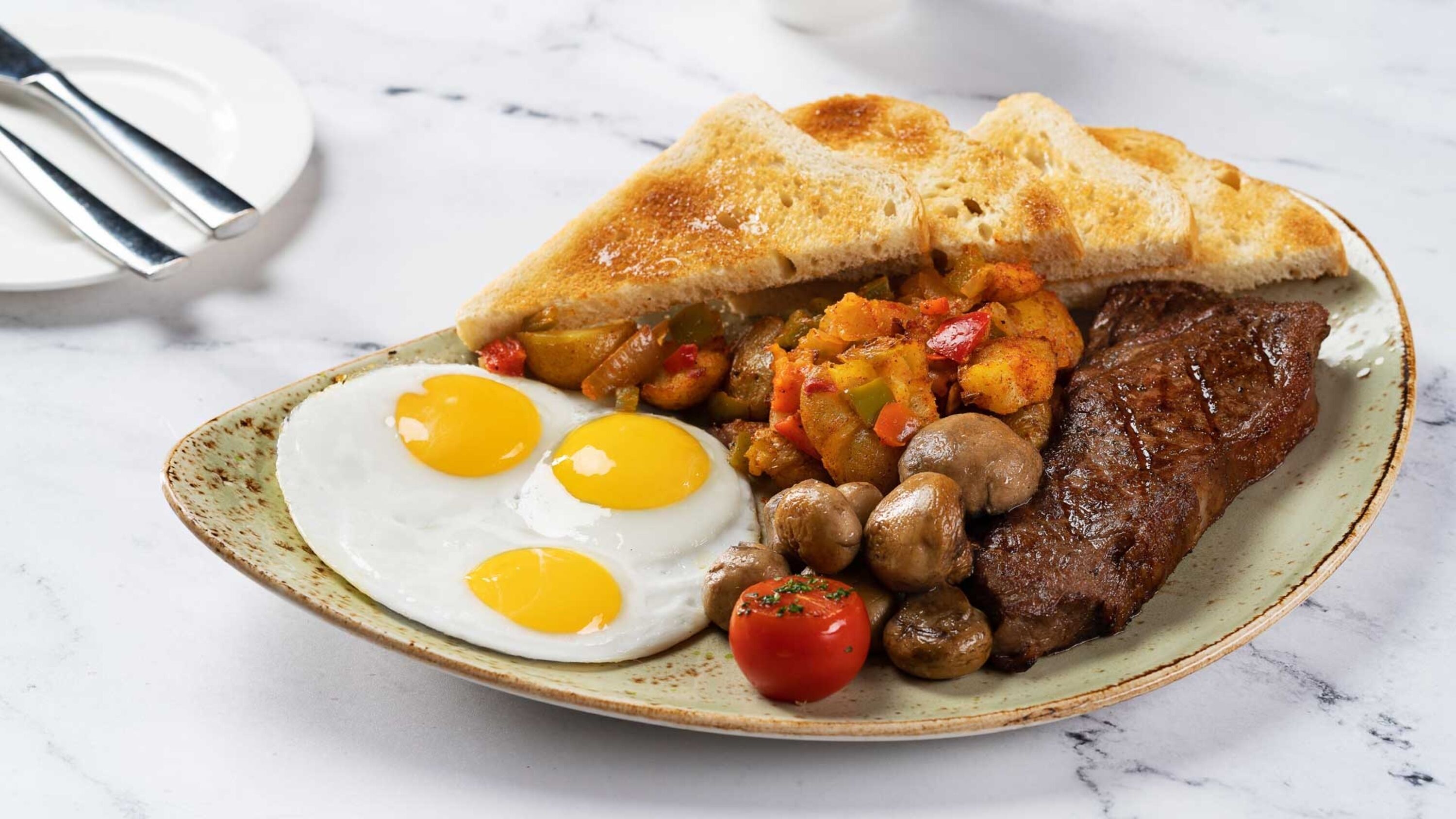 A plate with eggs, toast, steak, mushrooms, and vegetables.