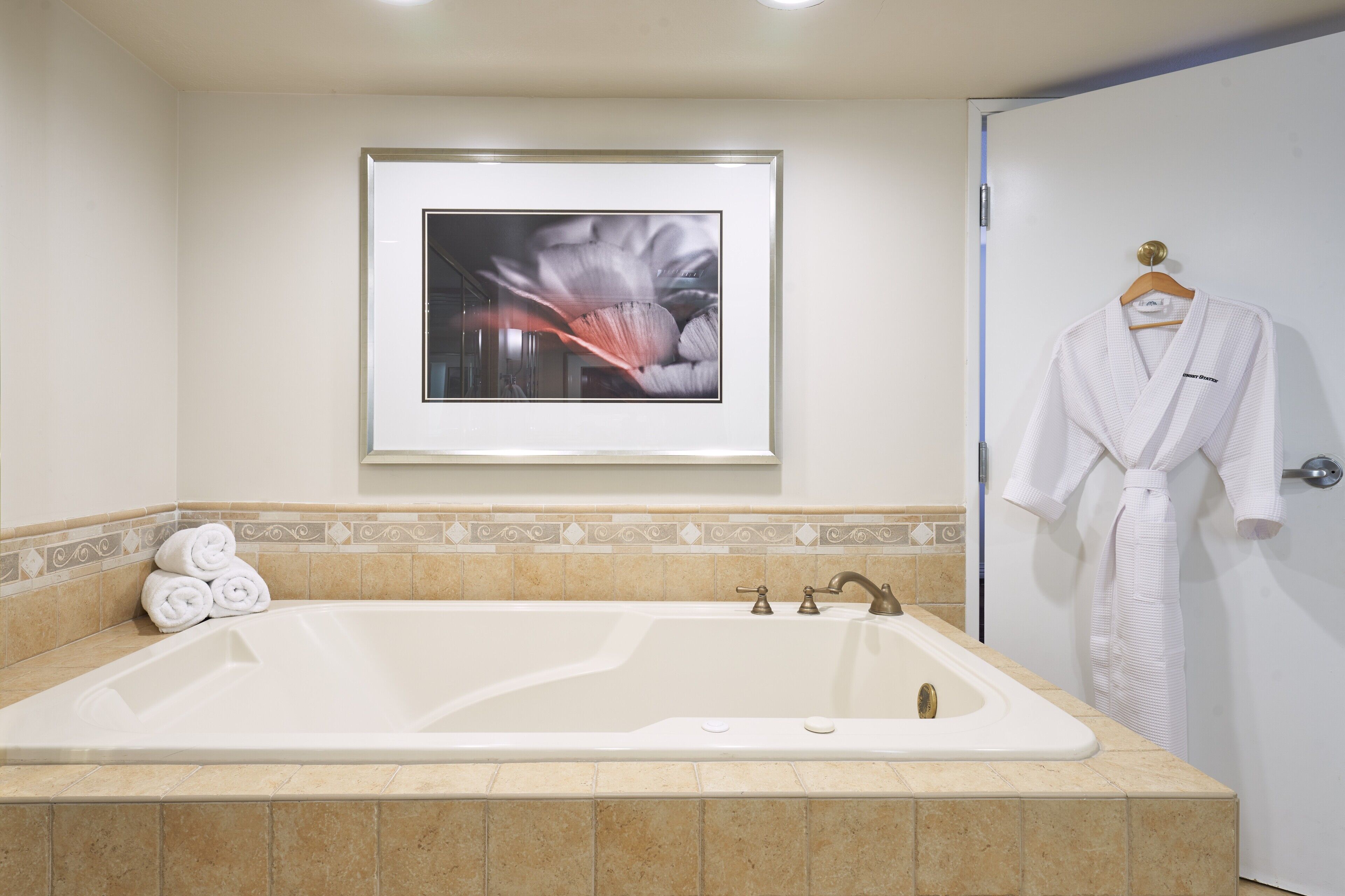 A bathroom with a large bathtub, a framed artwork on the wall, and a white robe hanging on the door.