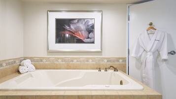 A bathroom with a large bathtub, a framed artwork on the wall, and a white robe hanging on the door.