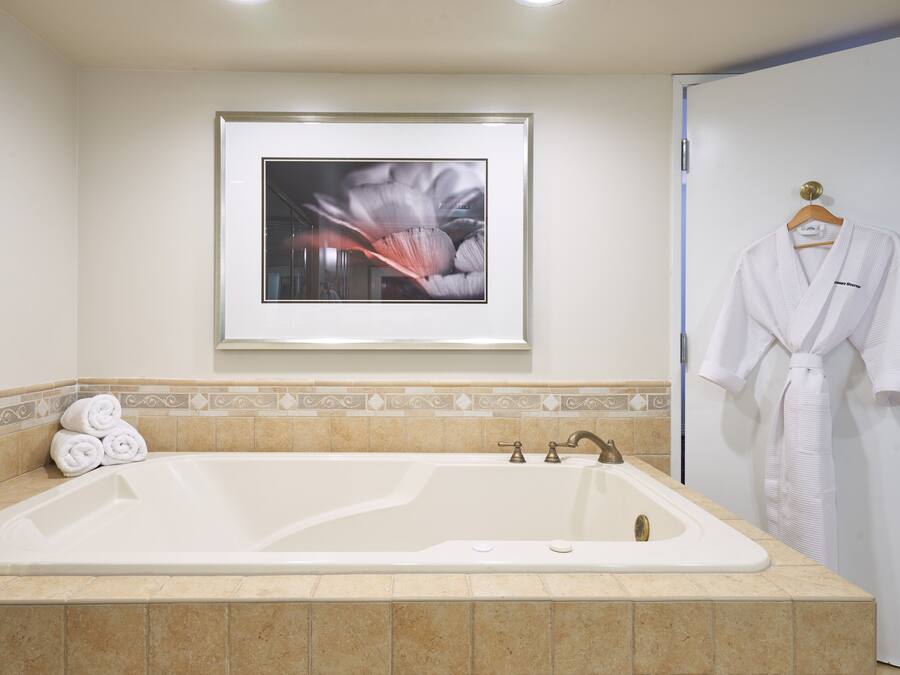 A bathroom with a large bathtub, a framed artwork on the wall, and a white robe hanging on the door.