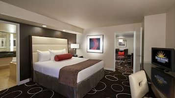 A hotel room with a large bed, a television, a desk with a chair, and a bathroom visible through an open door.