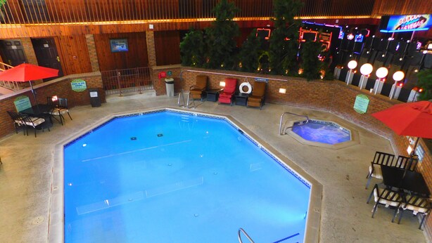 Una piscina interna con bordo piastrellato, una piccola vasca idromassaggio e diversi lettini e ombrelloni.