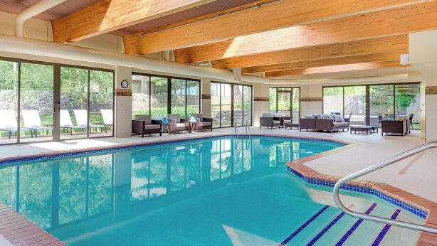 A swimming pool with clear blue water, surrounded by lounge chairs and sofas, large windows, and wooden ceiling beams. - Courtyard by Marriott in Portsmouth (Portsmouth)