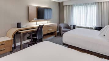 A hotel room with a bed, a desk with a chair, a television, and a window with curtains.