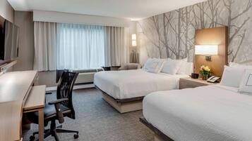 A hotel room with two beds, a desk, a chair, a TV, and a large window with curtains.