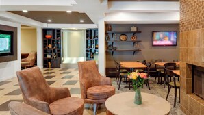 A modern lounge area with leather armchairs, a round table with a vase of flowers, and a television mounted on the wall. - Courtyard by Marriott in Portsmouth (Portsmouth)