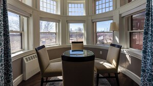 A bay window seating area with two chairs and a table, large windows, and a radiator. - The Centennial (Concord)
