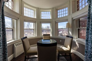 A bay window seating area with two chairs and a table, large windows, and a radiator. - The Centennial (Concord)