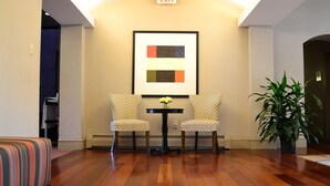 A lobby with two patterned chairs, a small table with a vase, a potted plant, and an exit sign. - The Centennial (Concord)