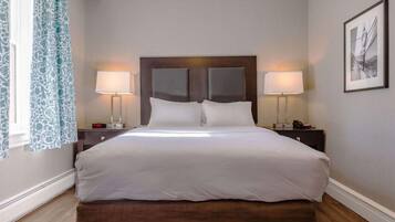 Una habitación de hotel con una cama grande, dos mesitas de noche, una lámpara y una ventana con cortinas, además de un cuadro en la pared.