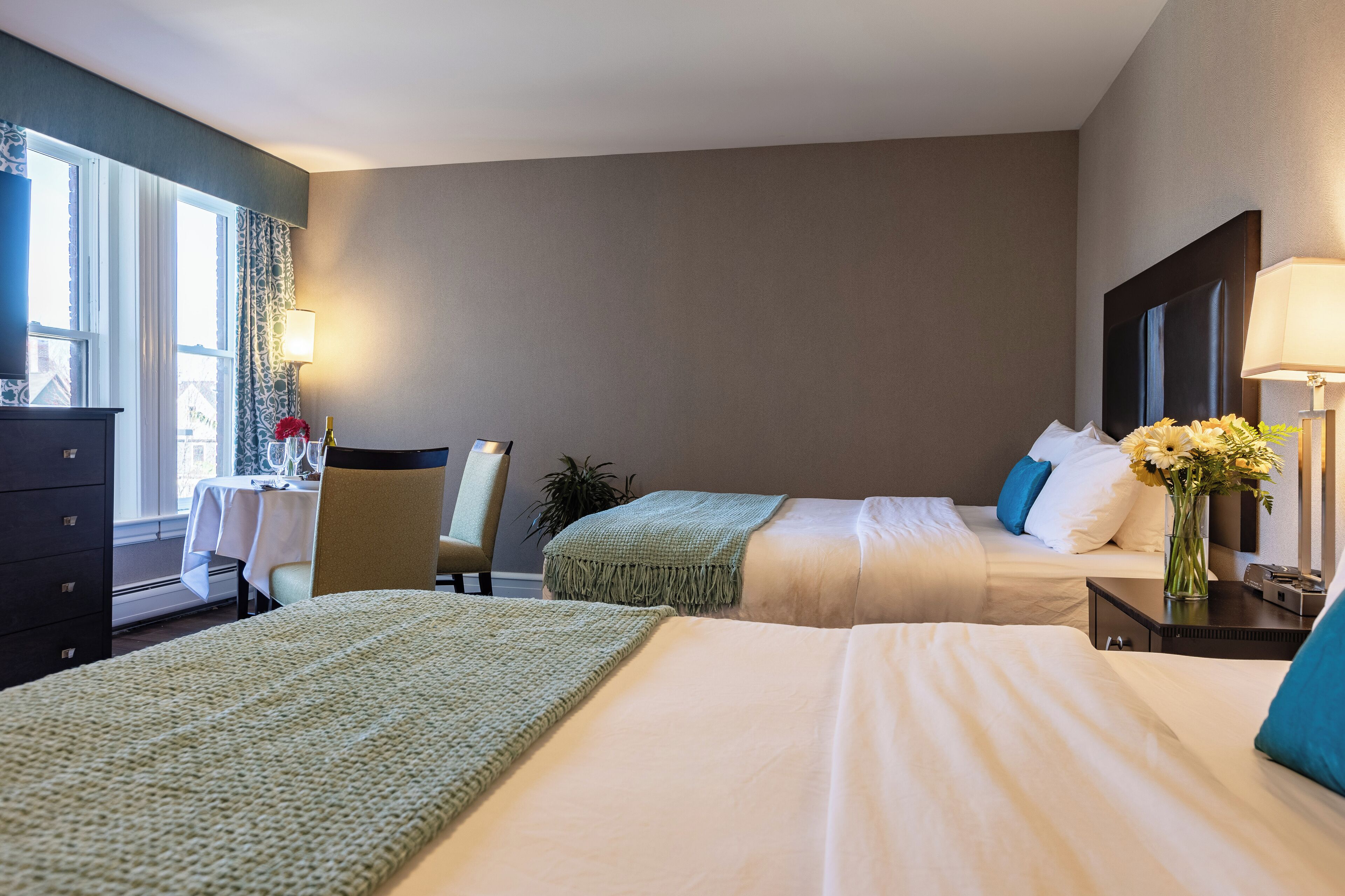 Habitación de hotel con dos camas, un escritorio, una silla, un aparador y una ventana con cortinas.