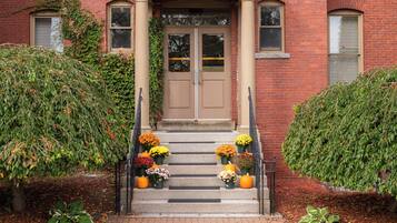 A brick building with a double door entrance, steps leading up to it, and a variety of potted plants and flowers on the steps.