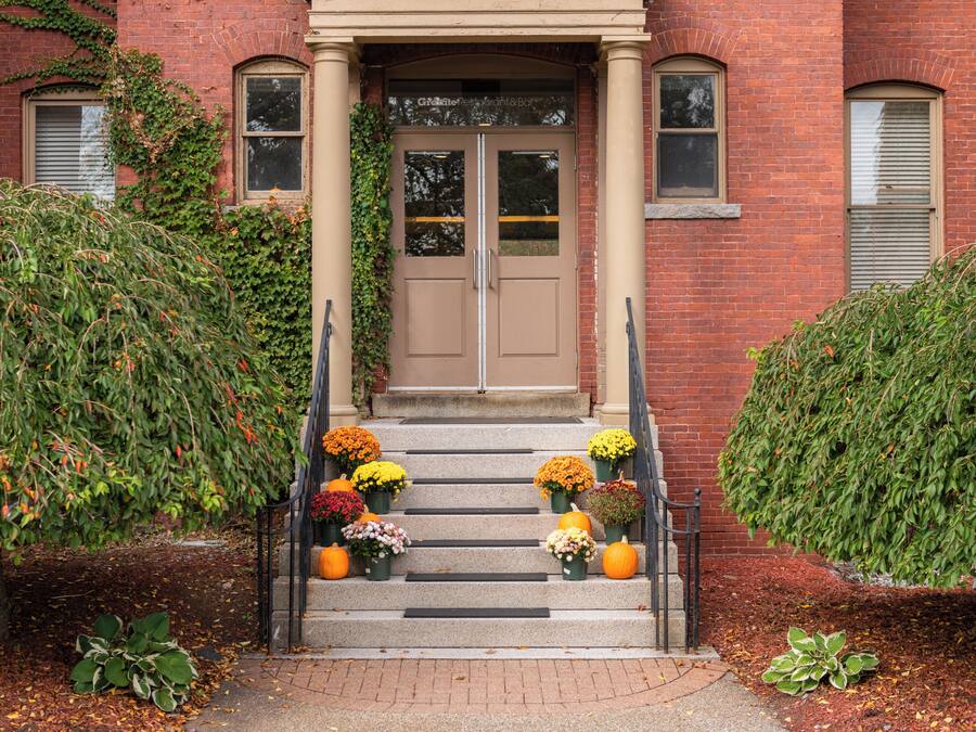 A brick building with a double door entrance, steps leading up to it, and a variety of potted plants and flowers on the steps.