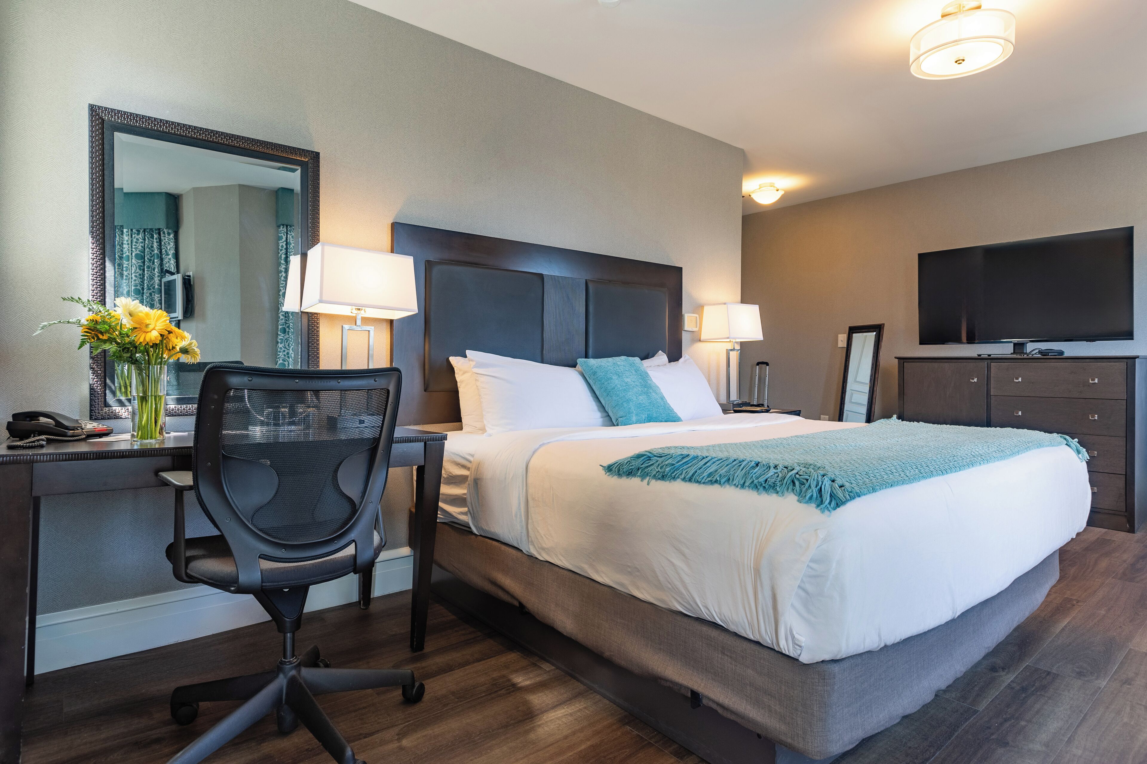 A hotel room with a bed, desk, chair, and a television.