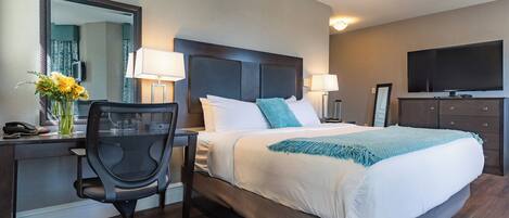 A hotel room with a bed, desk, chair, and a television.