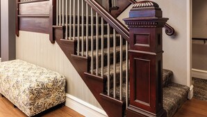A wooden staircase with a handrail, carpeted steps, and a bench at the bottom. - The Centennial (Concord)
