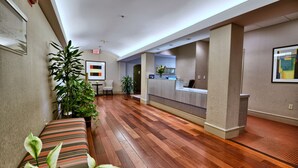 A hotel lobby with a reception desk, a bench, and potted plants. - The Centennial (Concord)