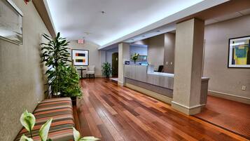 A hotel lobby with a reception desk, a bench, and potted plants.