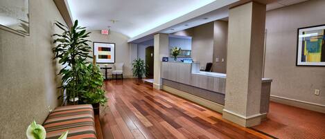 A hotel lobby with a reception desk, a bench, and potted plants.