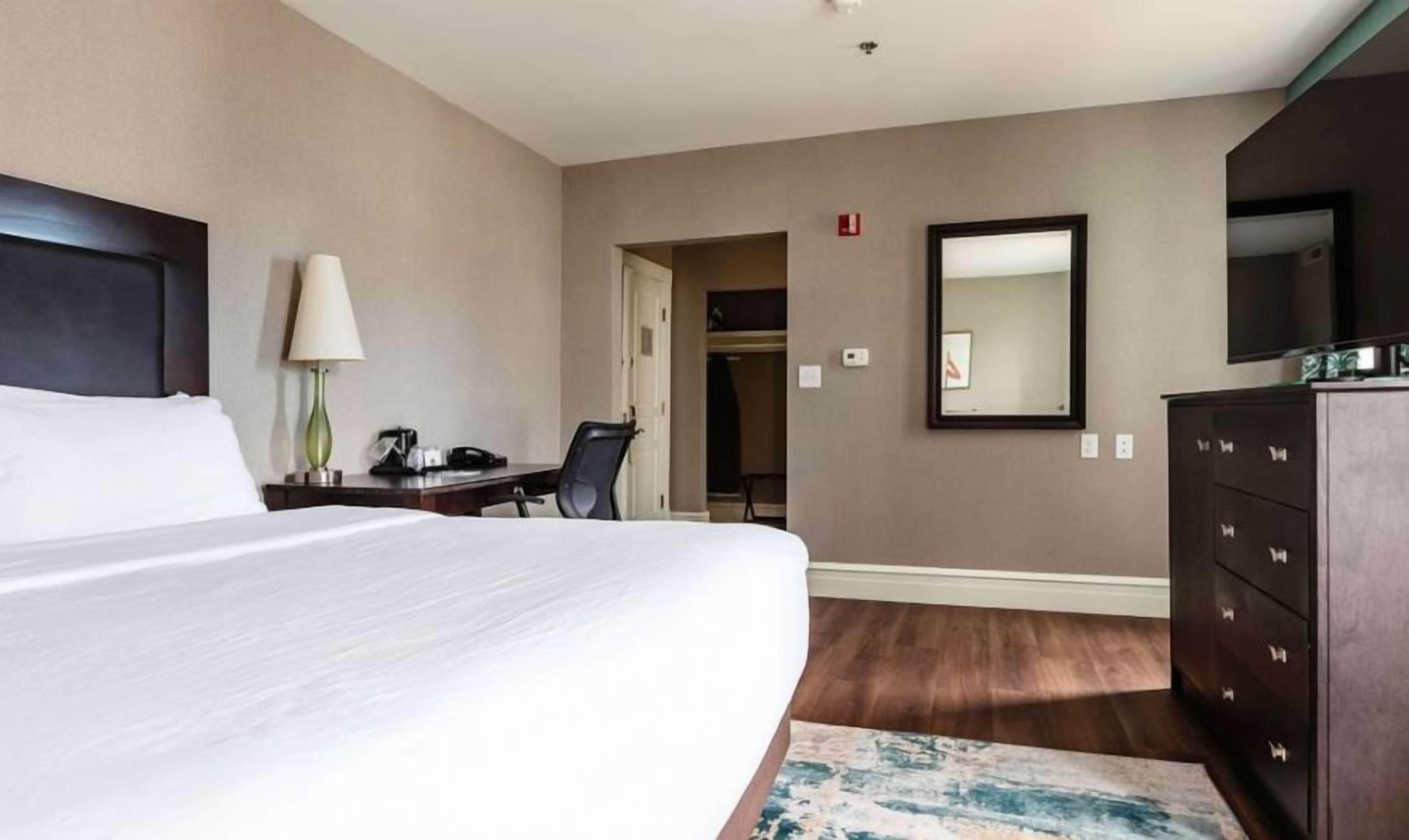 Habitació d'hotel amb un llit, escriptori, cadira, calaixera i mirall.