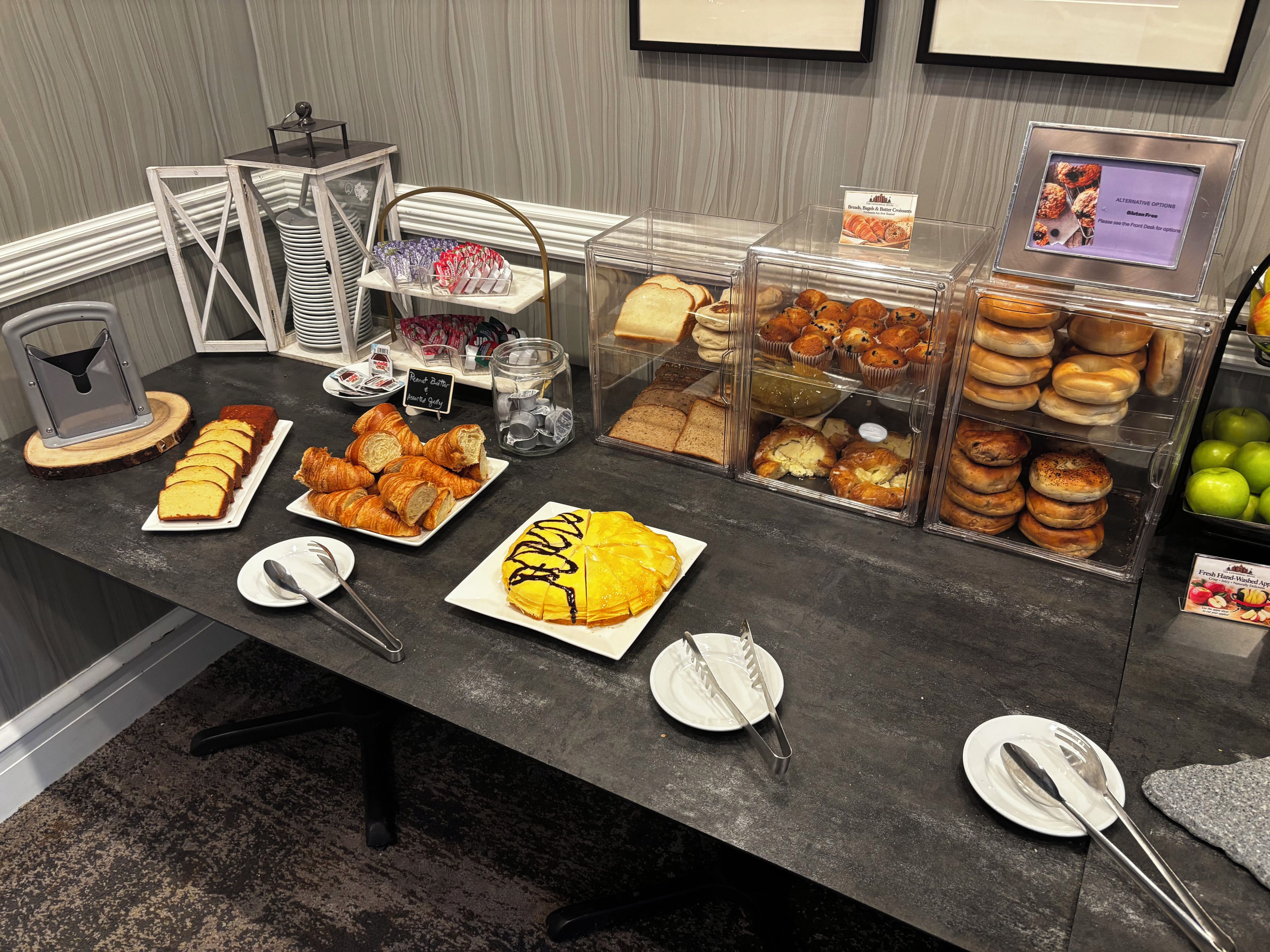 A buffet with various food items, including pastries and bread, arranged on a counter with serving utensils.