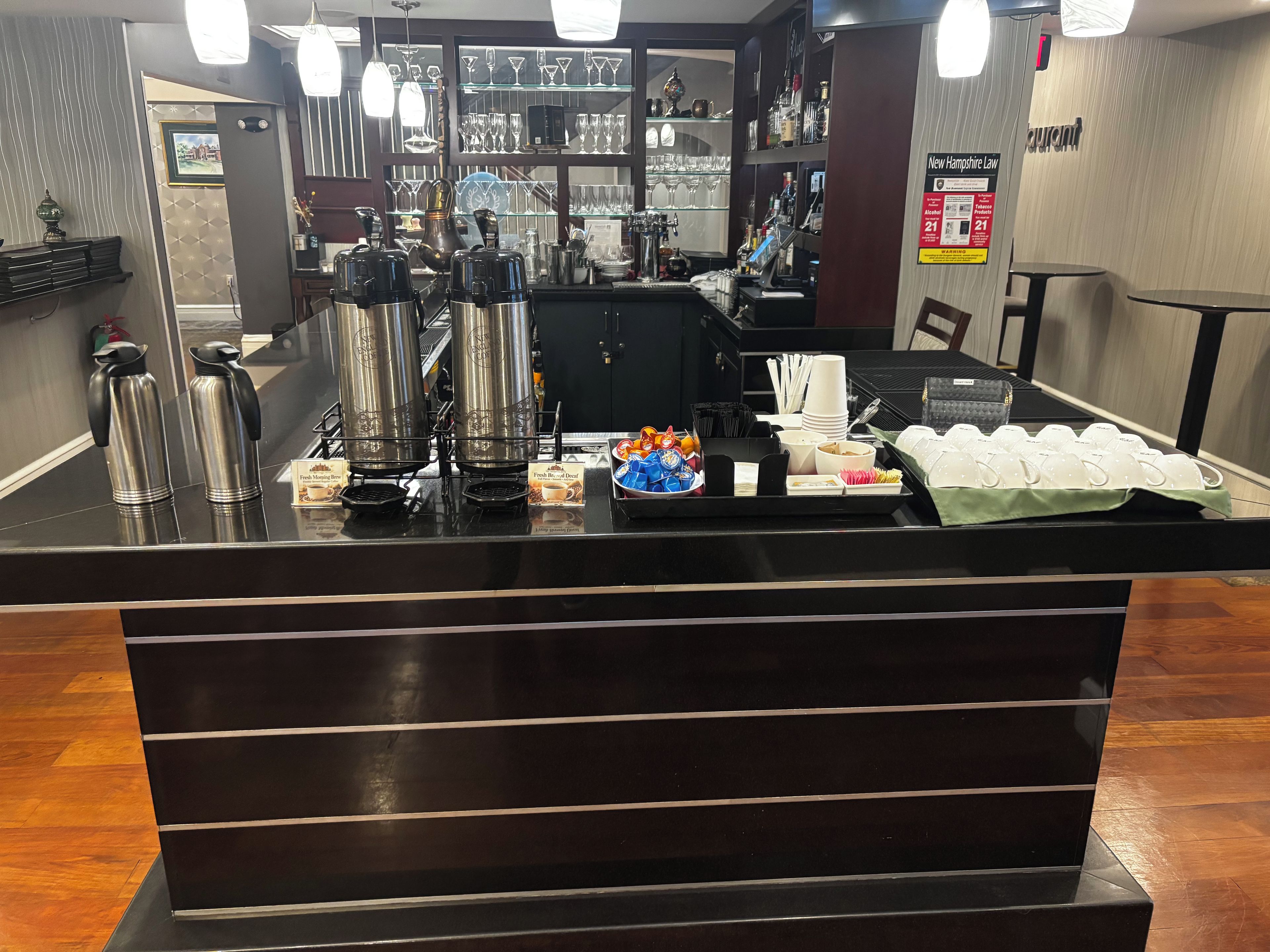 Área de bar com estação de café, copos e um quadro de menu.
