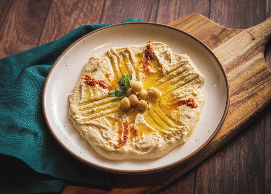 A plate of hummus with olive oil, chickpeas, and spices on a wooden board.