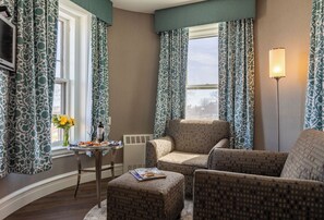 A cozy living room with patterned curtains, a comfortable sofa, a small table with a magazine, and a vase with flowers.