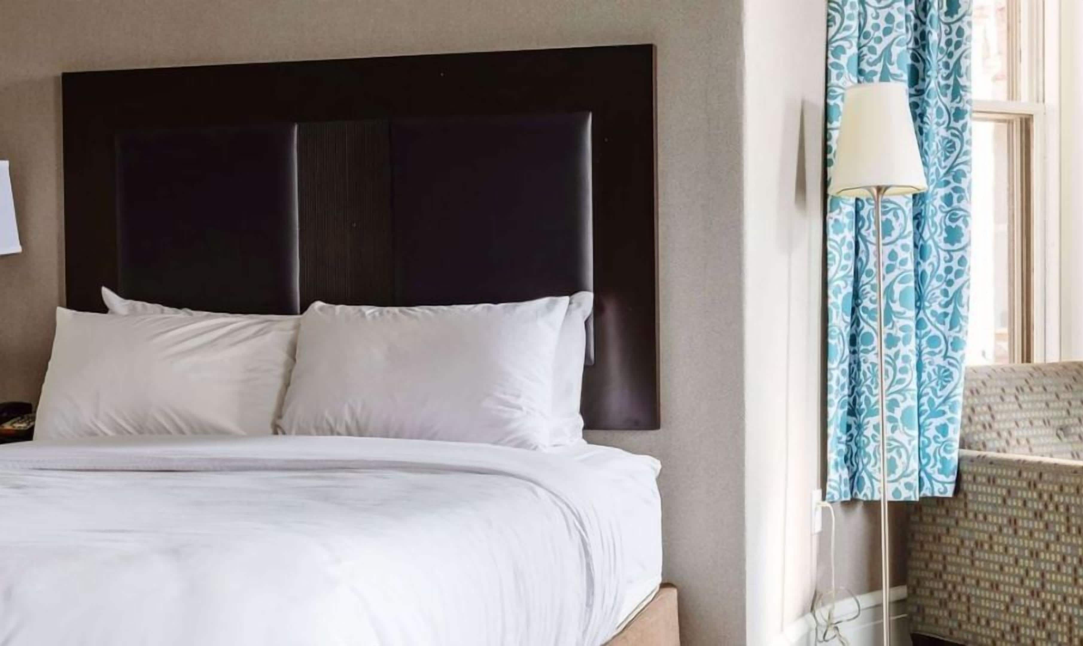 A hotel room with a large bed, a dark headboard, and a lamp by the window.