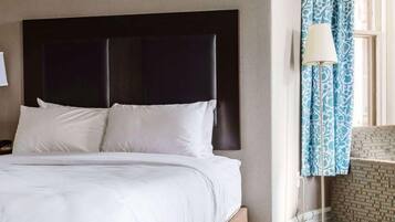 A hotel room with a large bed, a dark headboard, and a lamp by the window.