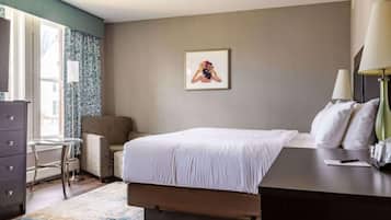 Een hotelkamer met een bed, een bureau, een stoel, een dressoir, een lamp en een lijst aan de muur.