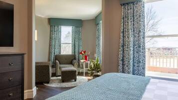 A hotel room with a bed, a chair, a small table with a vase, and a view of the outside.
