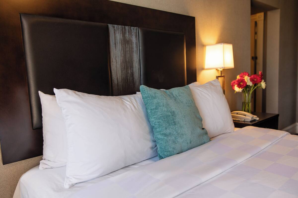A neatly made bed with a dark headboard, white and teal pillows, and a checkered bedspread.