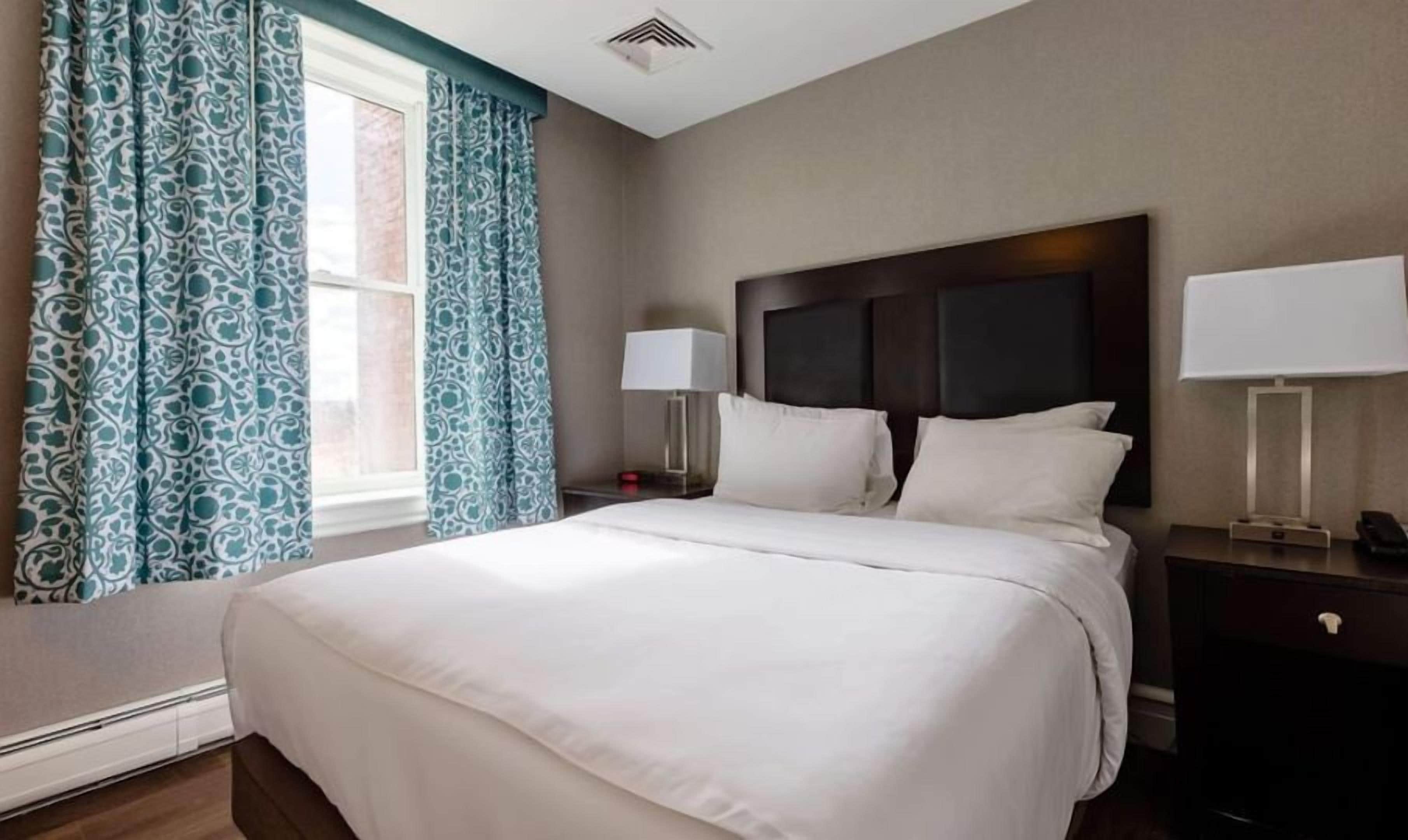 A hotel room with a large bed, two bedside tables, a nightstand, and a window with curtains.
